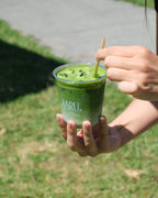 Person holding an iced matcha latte in a clear cup with a straw, outdoors.